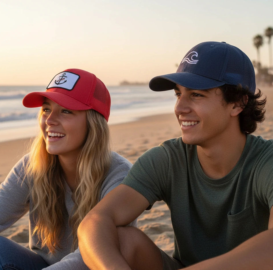 Two people sitting on a beach wearing baseball caps with sunset in the background